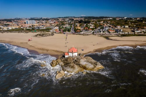 Vista aérea da capela de telhado vermelho em rocha isolada vista para praia de areia na propriedade costeira EcoHost, Portugal