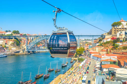 Teleférico de Gaia sobrevoando o Rio Douro com vista da paisagem histórica do Porto, suas pontes e edifícios com telhados vermelhos