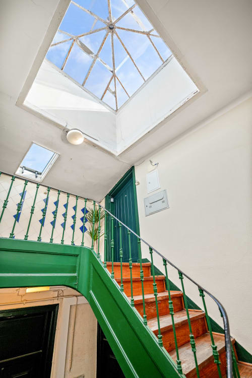 Escadaria moderna com corrimãos verdes e degraus laranja sob claraboia no 1898 Home & Suites em Lisboa