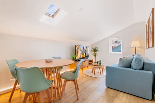 Área de estar moderna no 1898 Home & Suites, Lisboa, com mesa de jantar, sofá azul, assoalho em madeira e claraboia