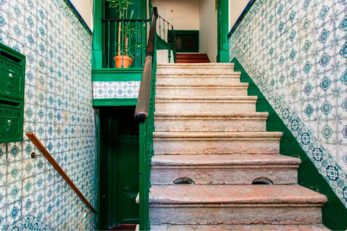 Escadaria do 1898 Home & Suites em Lisboa com corrimãos verdes, azulejos azuis padronizados e degraus de madeira