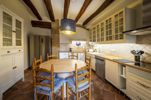 Amplia cocina de granja con vigas de madera, muebles color crema y mesa redonda con cojines azules en Estada Rural
