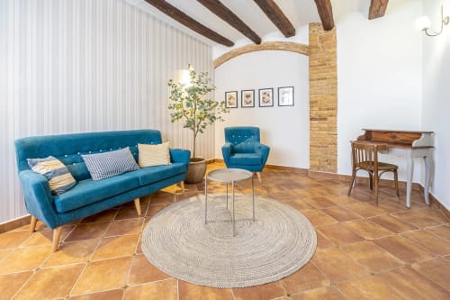 Luminoso salón rústico con sofá azul, alfombra redonda, vigas de madera vista y suelos de barro en Estada Rural