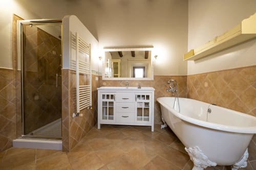 Baño de lujo con bañera exenta, tocador blanco, cabina de ducha acristalada y acabados en cerámica cálida en Estada Rural