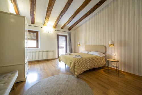 Amplio dormitorio rural en Estada Rural con vigas de madera vista, colcha con rayas amarillas y piso de madera
