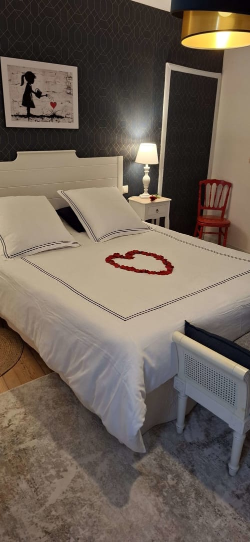 Suite romantique à La Cour Des Saligues avec lit blanc orné d'une décoration cœur, papier peint à motifs sombres et accents rouges