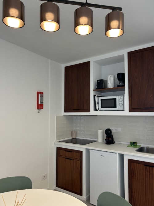 Pequeña cocina moderna en Kamalahouse, Corralejo: encimeras blancas, armarios de madera oscura, microondas e iluminación colgante