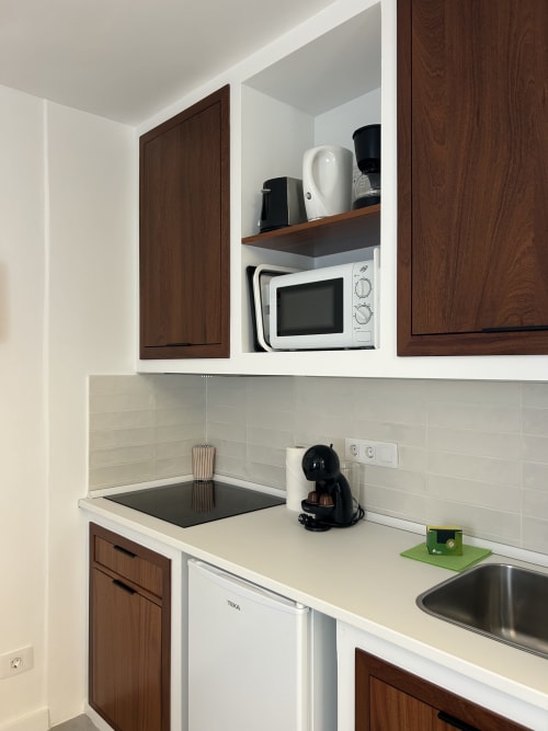 Rincón de cocina compacta en apartamento Kamalahouse SL en Corralejo con muebles de madera oscura, encimera blanca, microondas