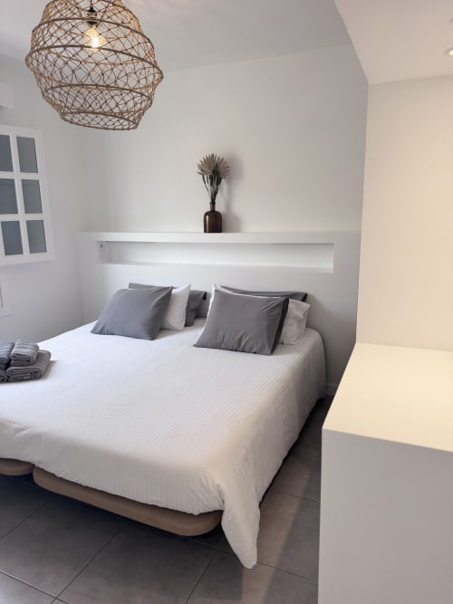 Dormitorio moderno en apartamento Kamalahouse, Corralejo: cama blanca, almohadas grises, lámpara colgante tejida y estante mural minimalista