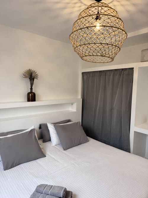 Dormitorio moderno en Kamalahouse de Corralejo con lámpara tejida, ropa de cama blanca, almohadas grises y decoración minimalista