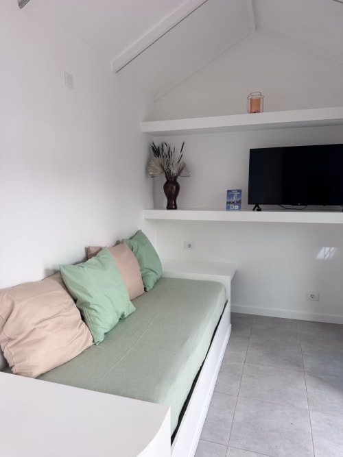 Dormitorio moderno en apartamento Kamalahouse, Corralejo con cama, almohadas verdes, estanterías empotradas, TV y decoración minimalista blanca