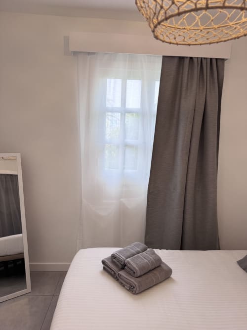 Dormitorio moderno con cama blanca, toallas dobladas, cortinas de gasa y marrón, lámpara colgante de mimbre en Kamalahouse, Corralejo