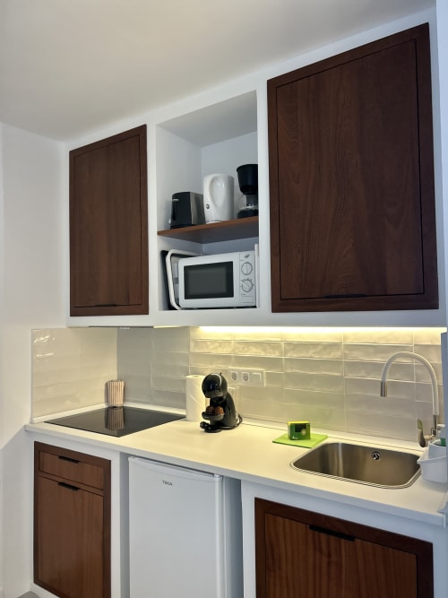 Cocina moderna en apartamento Kamalahouse, Corralejo, con muebles de madera oscura, encimeras blancas, microondas y acero inoxidable