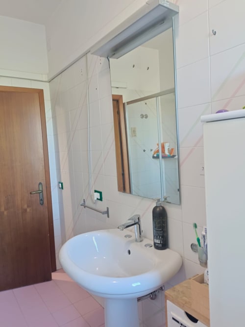 Modern bathroom with white pedestal sink, mirror, and tiled walls in Tales of Abruzzo apartment, Atessa