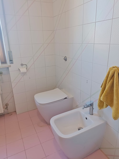 Clean bathroom in Tales of Abruzzo apartment, Atessa, with white toilet, bidet, sink, yellow towel, and tiled walls