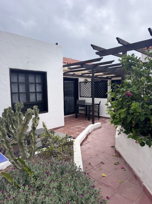 Patio de apartamento en Corralejo con terraza, pérgola, paredes blancas, ventanas negras y jardín mediterráneo