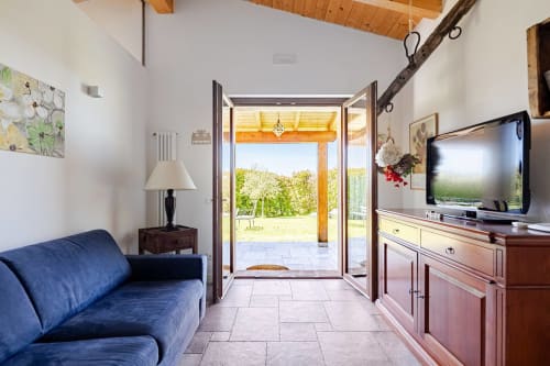 Bright living room at Casa Rossi Roma with blue sofa, open French doors to garden, wooden beams, and TV