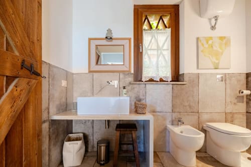 Modern bathroom at Casa Rossi Roma with white vessel sink, bidet, toilet, wooden cabinetry and terracotta tile accents