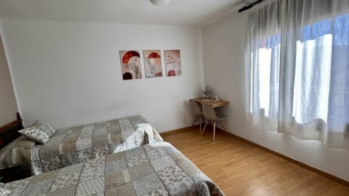 Bright double bedroom at Hostal Estació in Puigcerdà with wooden floors, patterned bedding, desk, and mountain views through