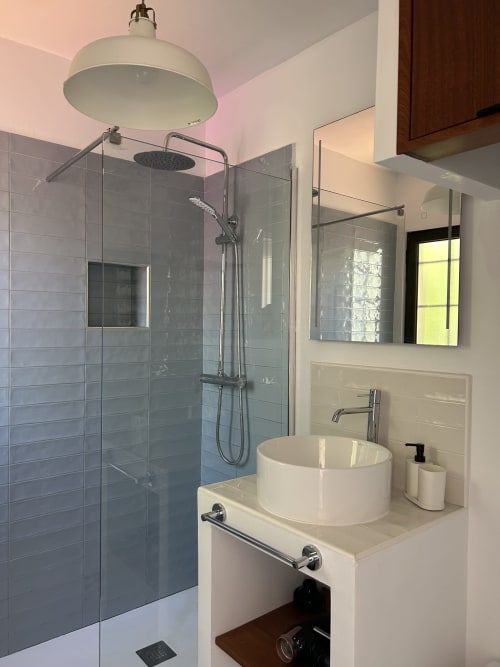 Baño moderno en apartamento Kamalahouse con ducha tipo lluvia, lavabo de cerámica blanca redondo, espejo y paredes con azulejos grises