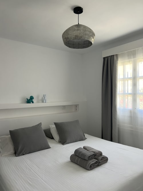 Dormitorio moderno en Kamalahouse de Corralejo con lámpara colgante, ropa de cama blanca, almohadas grises y toallas dobladas