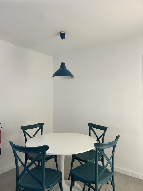 Comedor moderno de Kamalahouse con mesa redonda blanca y cuatro sillas color turquesa bajo una lámpara colgante