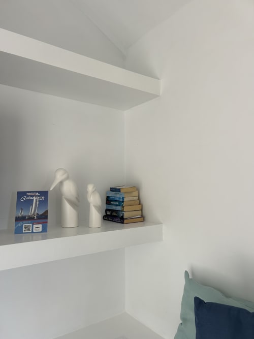 Estante blanco moderno con bustos decorativos blancos, libros apilados y folleto de viajes en el apartamento Kamalahouse, Corralejo