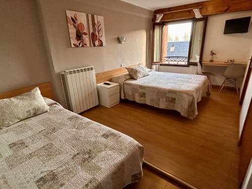 Triple bedroom at Hostal Estació in Puigcerdà with two beds, wooden flooring, and mountain views from window