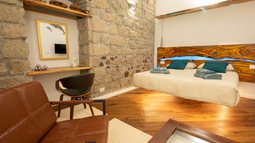 Nowoczesna sypialnia w Sardegna Explora House w Magomadas z łóżkiem drewnianym, kamiennymi ścianami, siedziskami ze skóry i drewnianym biurkiem.