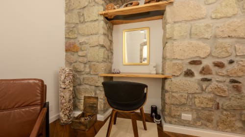 Przestrzeń robocza ze ścianami z kamienia w apartamencie Sardegna Explora House z drewnianym biurkiem, czarnym krzesłem i lustrem w złotej ramie