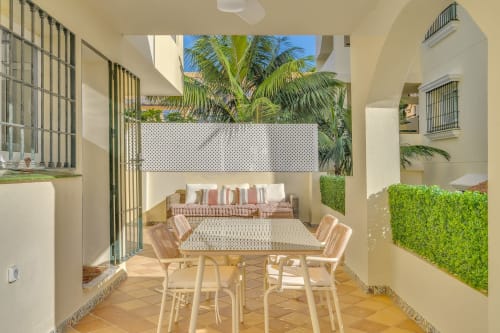 Sunny patio at HomyMarbella Elviria with dining table, lounge seating, and palm trees visible overhead