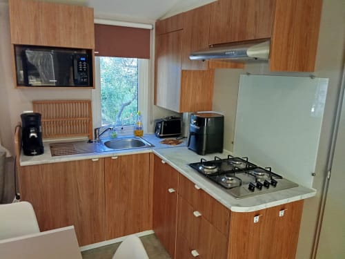 Petite cuisine du Mobil Home Magnolia au Camping La Lézardière avec placards bois, cuisinière gaz et vue sur le jardin