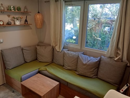 Espace de vie douillet du Mobil Home Magnolia au Camping La Lézardière avec sièges intégrés, vue sur jardin et mobilier moderne
