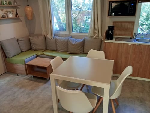 Mobil-home Magnolia : séjour avec table à manger, chaises crème, canapé d'angle et vue sur le jardin au Camping La Lézardière