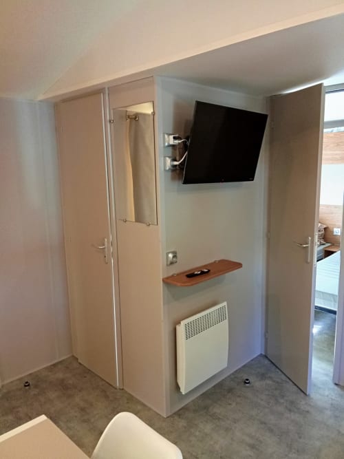 Intérieur de mobil-home au Camping La Lézardière avec TV murale, étagère en bois, radiateur et mobilier moderne