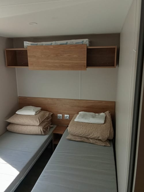 Chambre à deux lits simples du Mobil Home Magnolia au Camping La Lézardière, La Valette du Var avec tête de lit en bois et literie beige