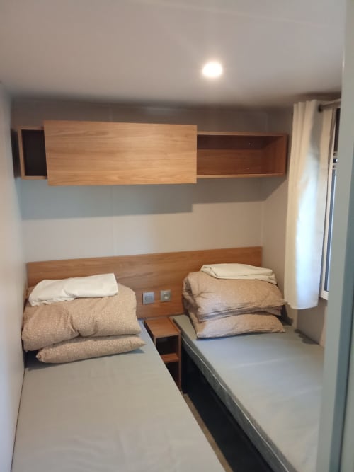 Chambre Mobil Home Magnolia avec deux lits simples, têtes de lit en bois et rangements à Camping La Lézardière, La