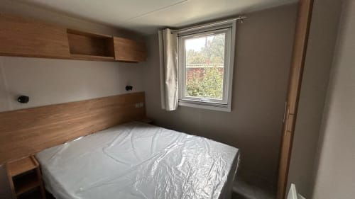 Chambre du mobil-home du Camping La Lézardière avec lit double, tête de lit en bois, fenêtre donnant sur le jardin et rangements intégrés.