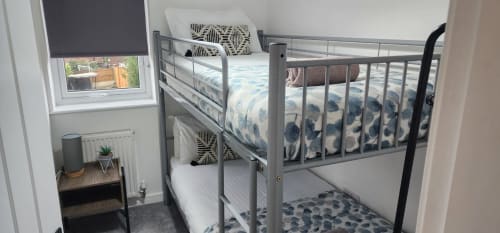Metal bunk beds with blue bedding in bright bedroom with window, radiator, and small side table at Ideal Home Away property
