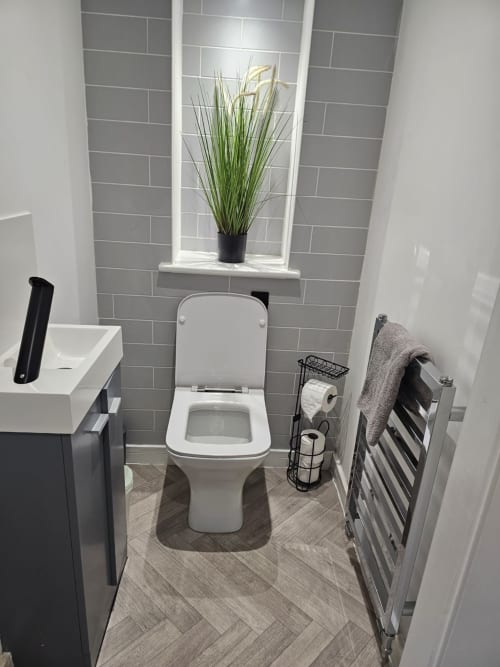 Modern bathroom in Radcliffe N6 house with white toilet, gray tile walls, and decorative plant on window ledge.