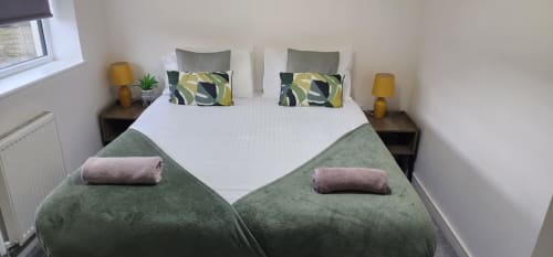 Modern bedroom with twin beds, green throws, patterned pillows, bedside lamps and tables at Radcliffe N6 holiday home in
