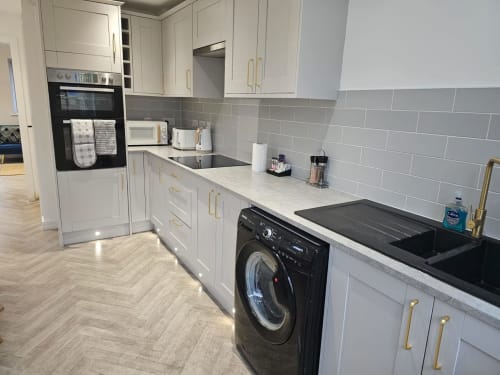 Modern kitchen with white cabinetry, gray subway tile backsplash, black washing machine, and black sink in Radcliffe N6