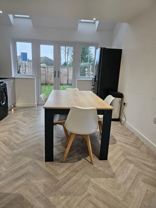 Modern kitchen-diner with wooden dining table, cream chairs, black appliances, and bi-fold doors opening to fenced garden at