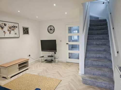 Modern living area with TV, wooden floor, yellow rug, and carpeted staircase in Radcliffe N6 holiday home