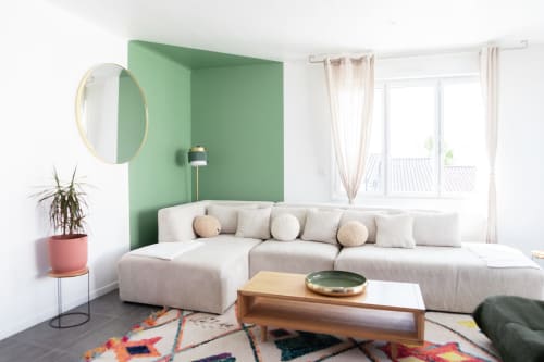 Salon moderne de la Villa Rompsay à La Rochelle avec canapé sectionnel crème, mur d'accent vert et tapis coloré