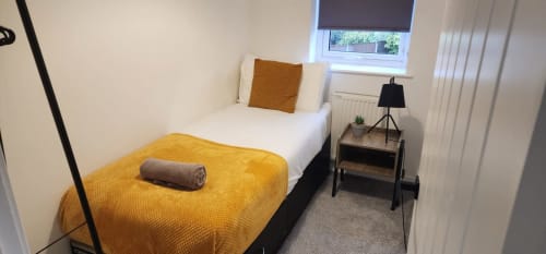 Modern bedroom in Radcliffe N6 apartment with single bed, yellow blanket, bedside table with lamp, window with garden view,