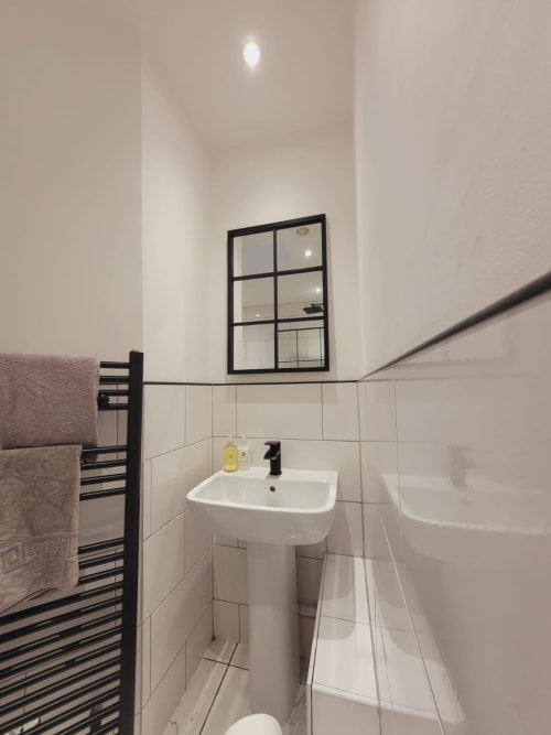 Modern bathroom with pedestal sink, white tiles, black framed mirror, heated towel rack, and toilet in Radcliffe N6