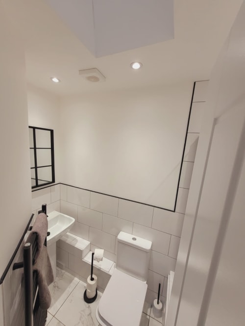 Modern bathroom with white tiles, toilet, sink, black framed mirror and towel rack in Radcliffe N6 apartment