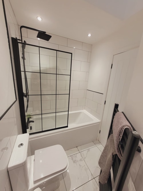 Modern bathroom with white subway tiles, black-framed shower enclosure over bathtub, white toilet, and towel rack at
