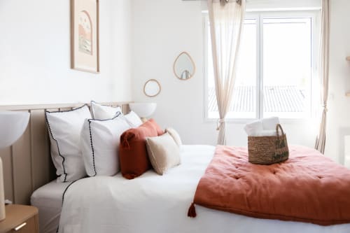 Chambre lumineuse de la Villa Rompsay ARLOÉ à La Rochelle, avec lit blanc, jeté matelassé corail, miroirs décor et beige